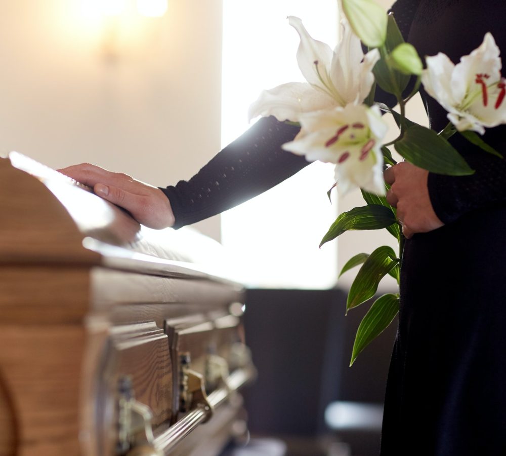 woman-with-lily-flowers-and-coffin-at-funeral.jpg